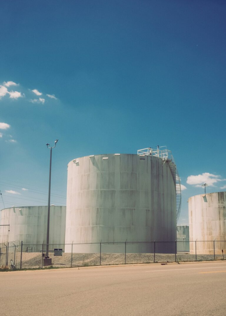 A person wearing gloves checks a large outdoor chemical storage tank for signs of leakage or damage.