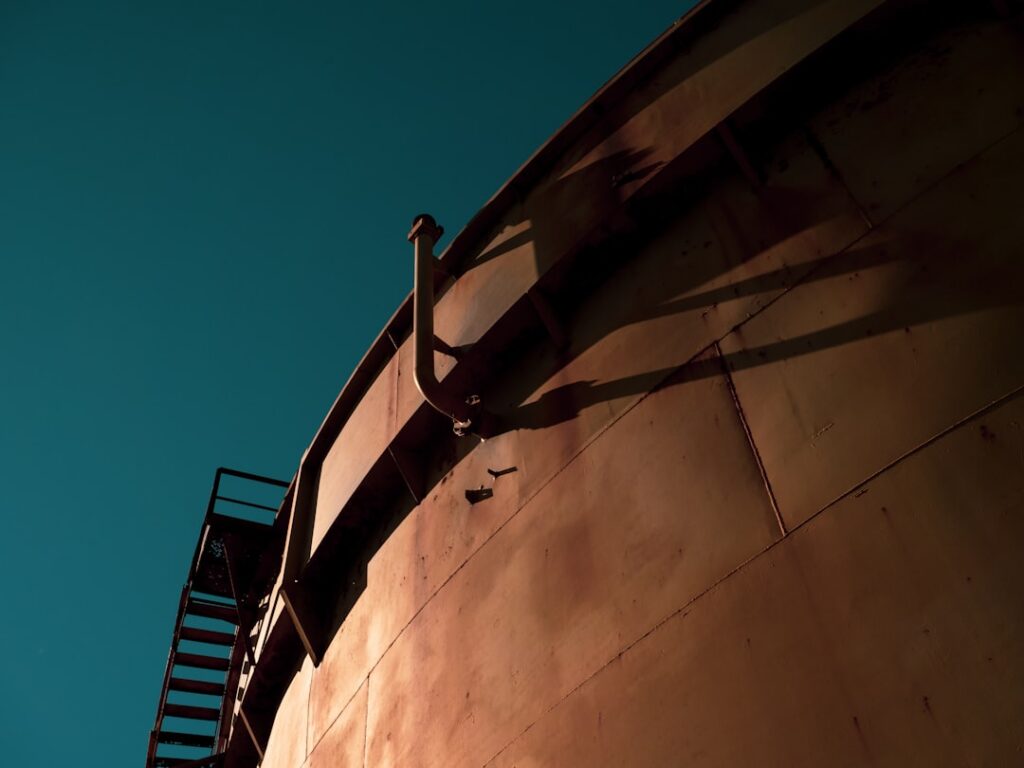 A person inspecting the exterior of a large outdoor chemical storage tank with gloves and protective gear.